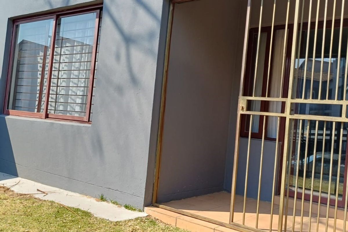 Rear exterior view of the apartment featuring a tiled patio area, sliding glass doors with security gates, and a sliding window.