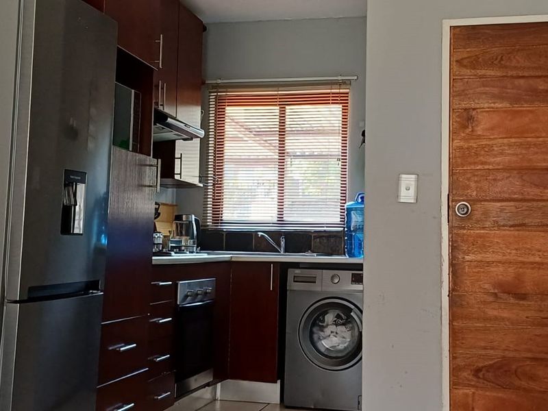 Compact kitchen featuring dark wood cabinetry, built-in oven and hob, extractor fan, and integrated laundry appliance space.