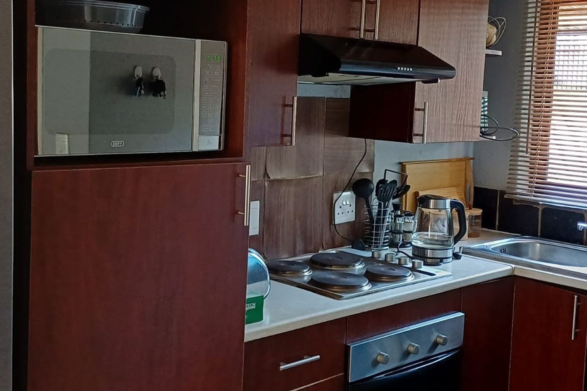 Compact kitchen featuring dark wood cabinetry, integrated appliances including an oven and hob, and a stainless steel sink with window views.