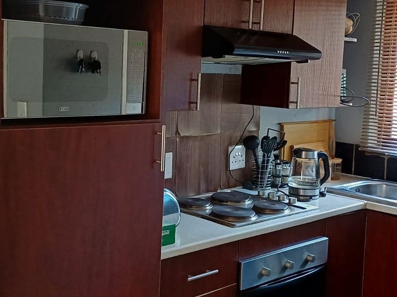 Compact kitchen featuring dark wood cabinetry, integrated appliances including an oven and hob, and a stainless steel sink with window views.
