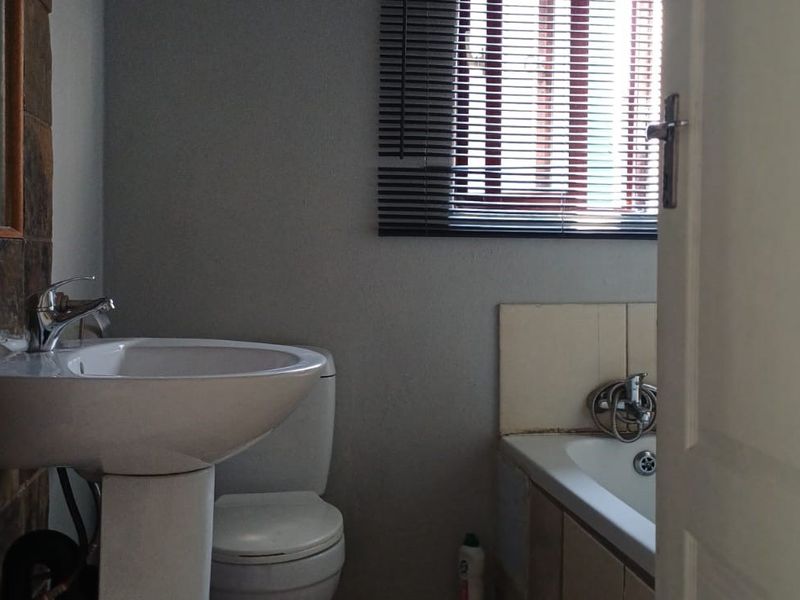 A functional bathroom featuring a pedestal basin, toilet, and bathtub with tiled splashback and venetian blinds.