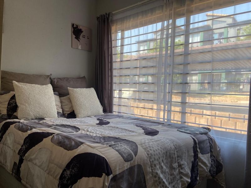 A bedroom featuring a large window with sheer and block-out curtains, providing natural light and a view of the exterior.