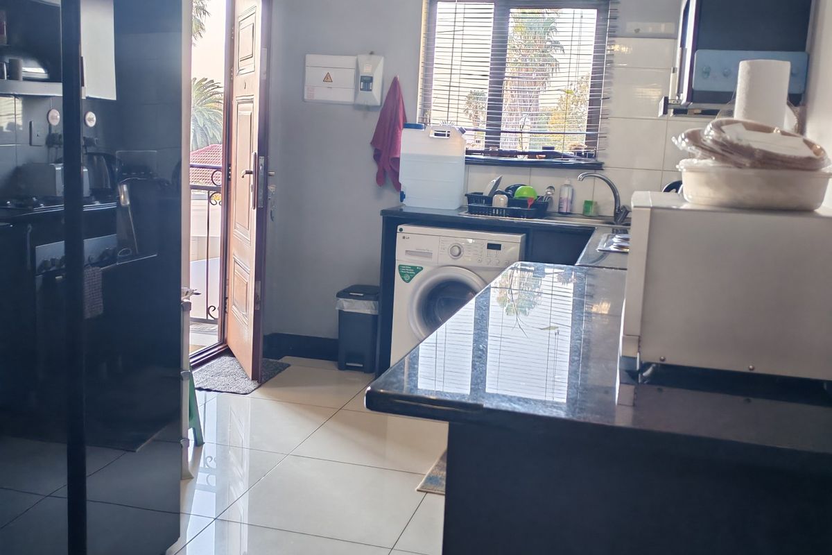 A functional kitchen featuring dark cabinetry, granite countertops, tiled flooring, and integrated laundry plumbing with direct access to an outdoor balcony area.