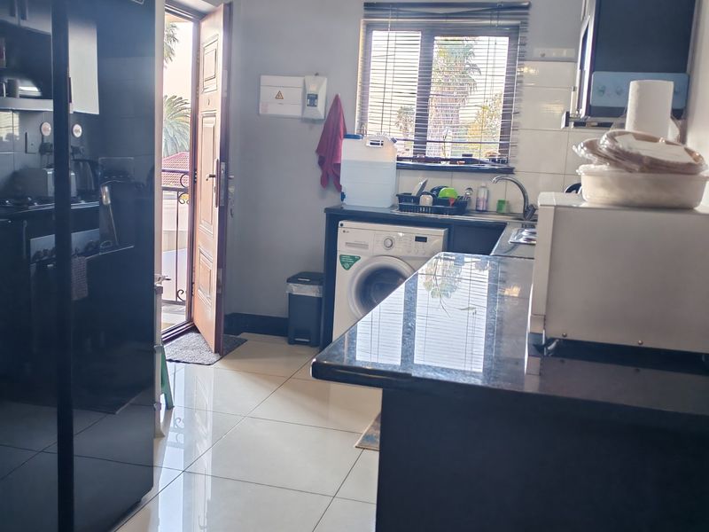 A functional kitchen featuring dark cabinetry, granite countertops, tiled flooring, and integrated laundry plumbing with direct access to an outdoor balcony area.