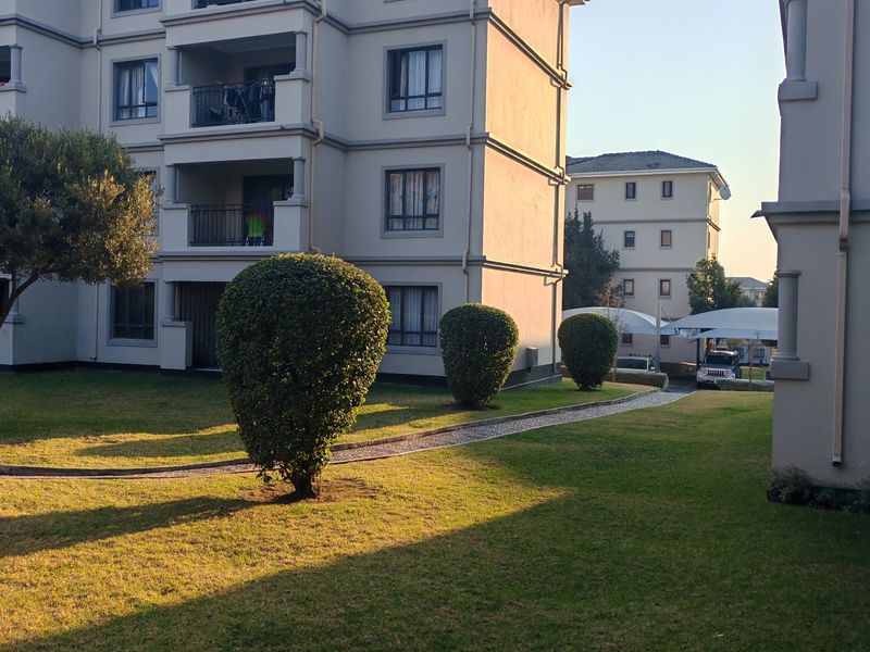 Exterior view of a multi-story apartment complex featuring private balconies, a well-maintained communal garden, and paved walkways.