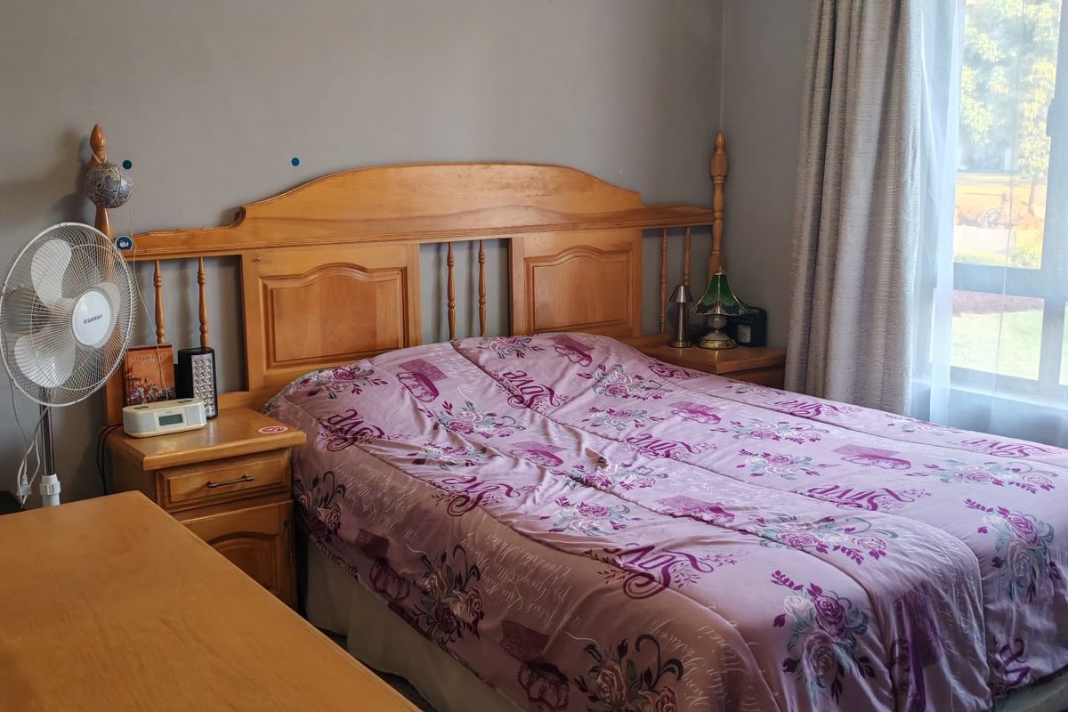A functional bedroom featuring tiled flooring and natural light from a large window with curtain tracks installed.