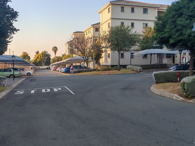 Exterior view of an apartment complex featuring paved driveways, covered parking bays, and landscaped grounds.