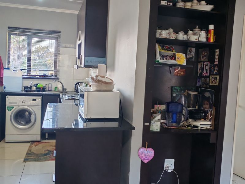 A functional kitchen featuring dark cabinetry, granite countertops, integrated laundry appliances, and a built-in shelving unit, finished with tiled flooring.
