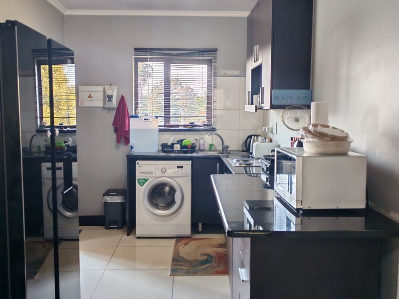 A functional kitchen featuring dark cabinetry, granite countertops, tiled flooring, and a built-in washing machine, offering a practical layout for daily use.