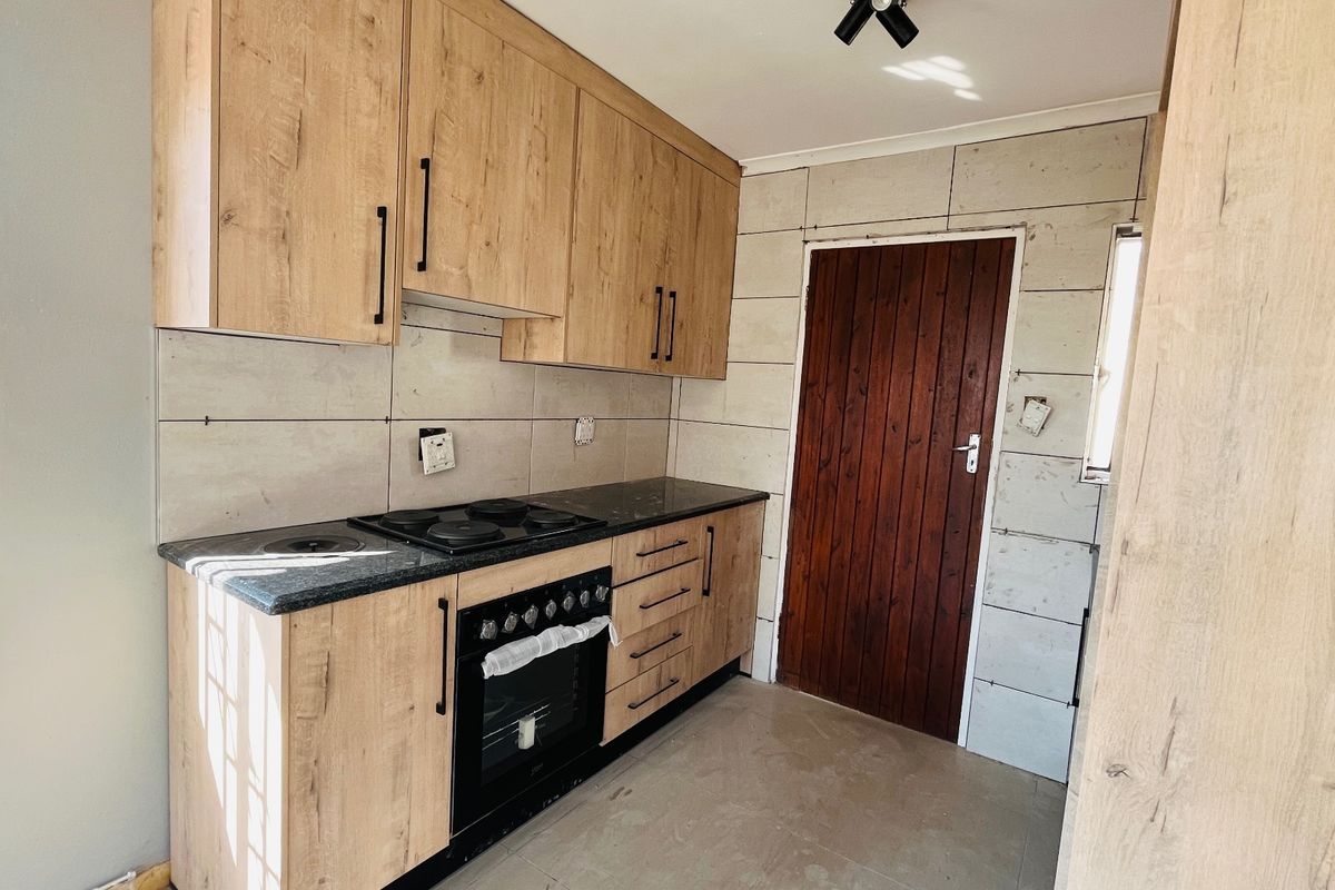 A functional kitchen featuring light wood-finish cabinetry, a built-in oven and hob, and stone countertops, currently awaiting final finishing touches.