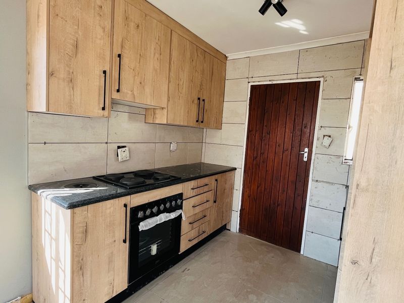 A functional kitchen featuring light wood-finish cabinetry, a built-in oven and hob, and stone countertops, currently awaiting final finishing touches.