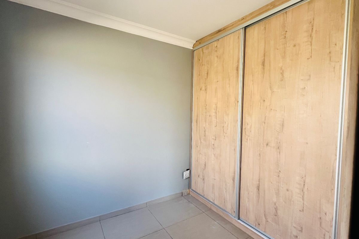 A clean, empty bedroom featuring neutral wall paint, tiled flooring, and a modern built-in sliding door wardrobe with a wood-grain finish.