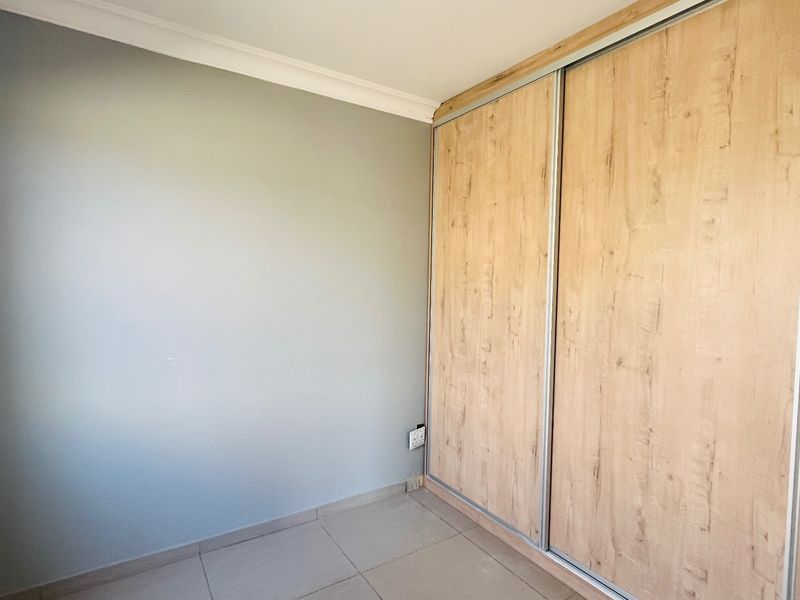 A clean, empty bedroom featuring neutral wall paint, tiled flooring, and a modern built-in sliding door wardrobe with a wood-grain finish.