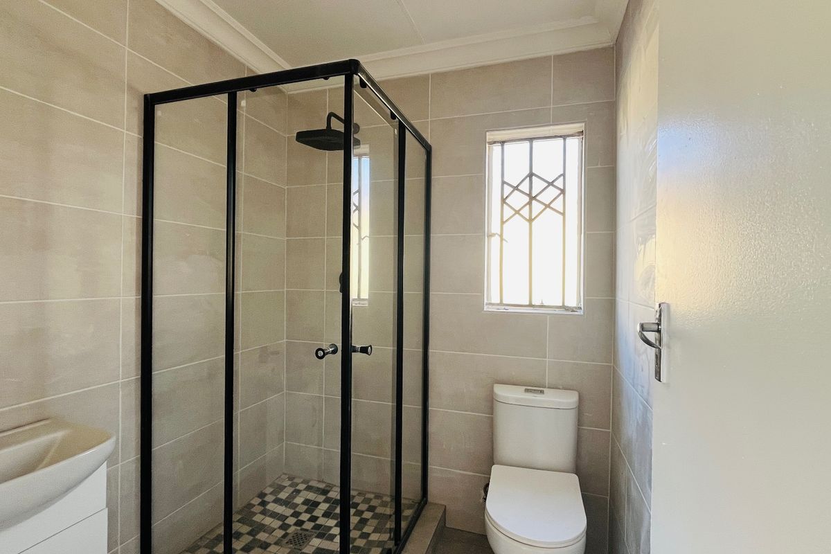A modern bathroom featuring a walk-in shower with black frame, wall-mounted basin, and toilet, finished with neutral wall tiles and contemporary black fixtures.