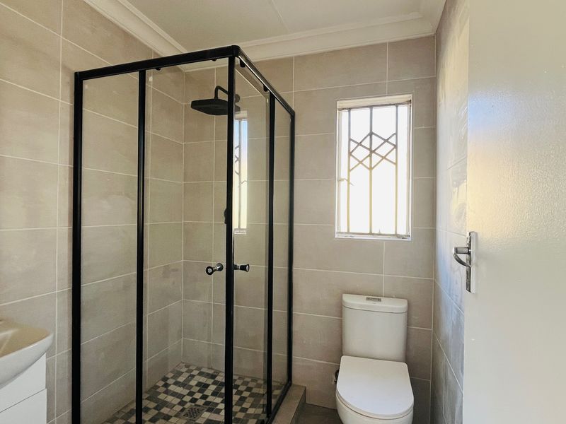 A modern bathroom featuring a walk-in shower with black frame, wall-mounted basin, and toilet, finished with neutral wall tiles and contemporary black fixtures.
