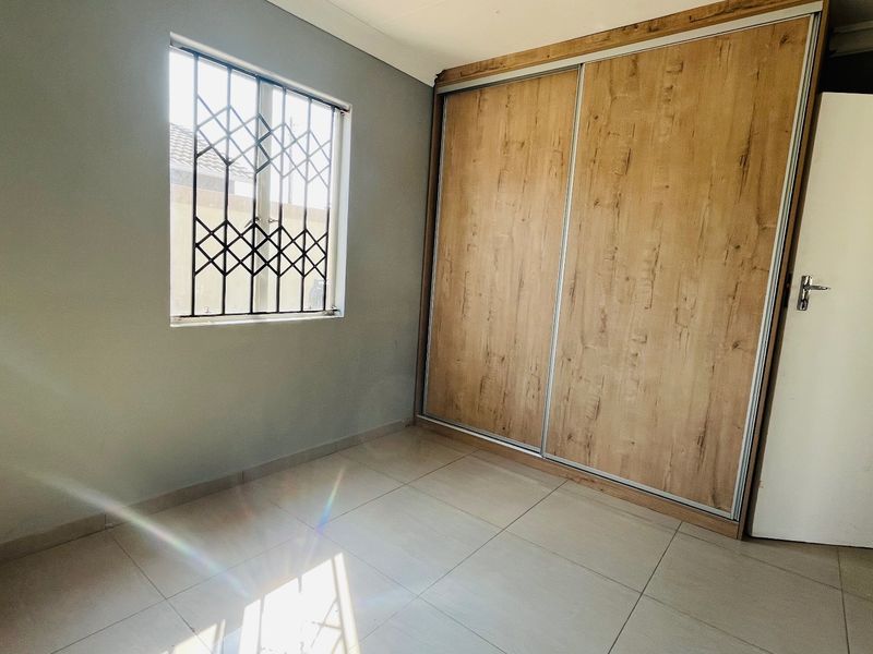 A bright, empty bedroom featuring neutral tiled flooring and a modern wood-finish built-in wardrobe with sliding doors.