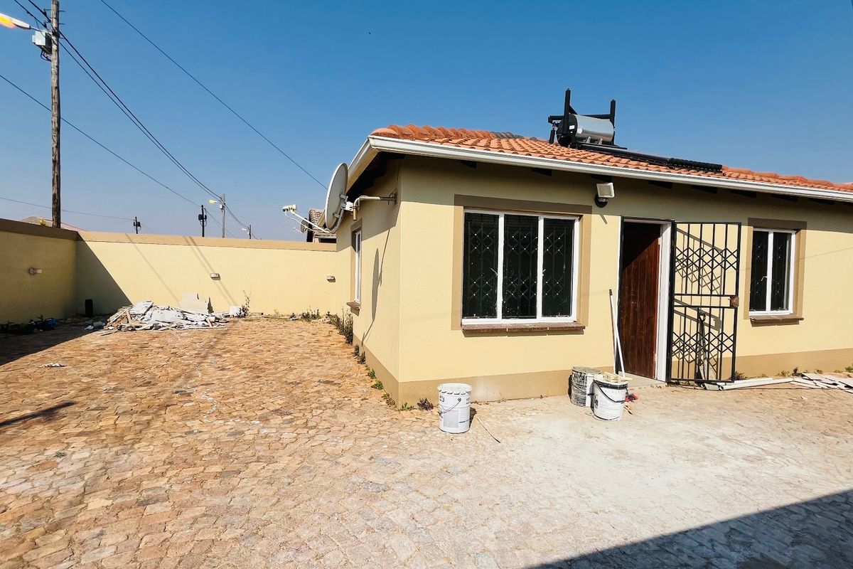 Rear view of a single-story house featuring a paved courtyard, terracotta roof tiles, and a solar water heating system.