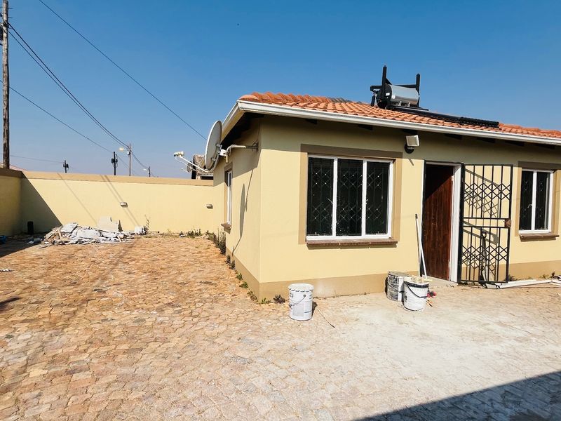 Rear view of a single-story house featuring a paved courtyard, terracotta roof tiles, and a solar water heating system.