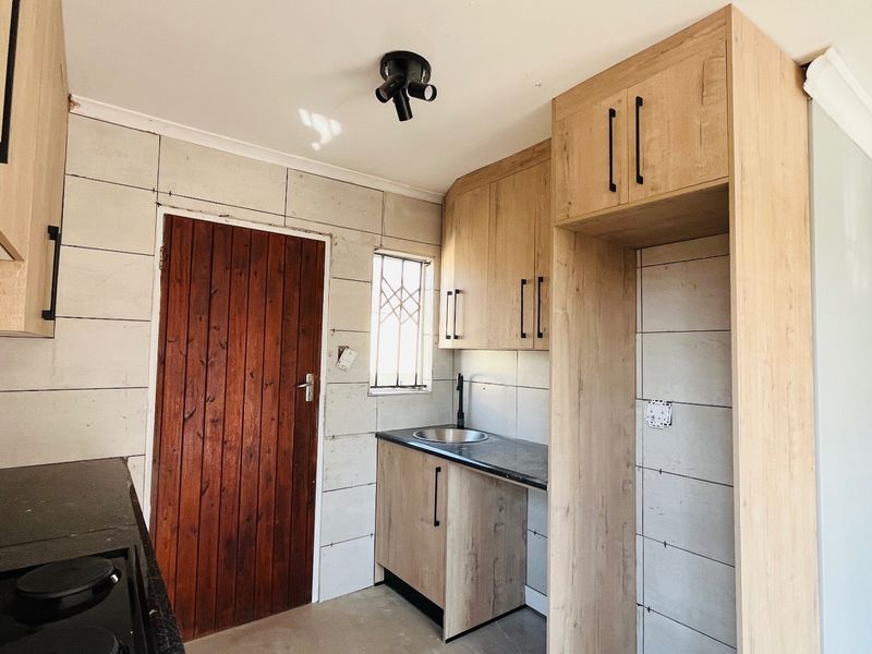 A compact kitchen featuring light wood-look cabinetry, dark countertops, a stainless steel sink, and a built-in hob, currently awaiting final finishing touches.