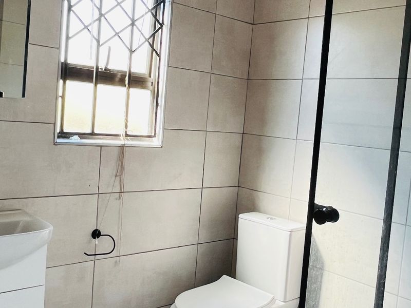 A functional bathroom featuring a modern toilet, vanity unit, and a glass-enclosed shower with neutral wall and floor tiling.