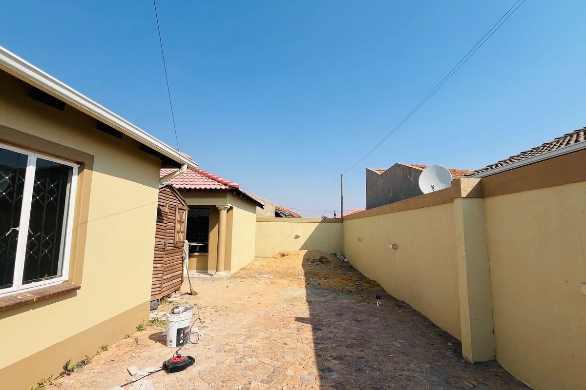 A rear exterior area featuring a perimeter wall and security bars on the window, currently requiring landscaping and surface finishing.