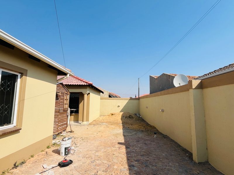 A rear exterior area featuring a perimeter wall and security bars on the window, currently requiring landscaping and surface finishing.