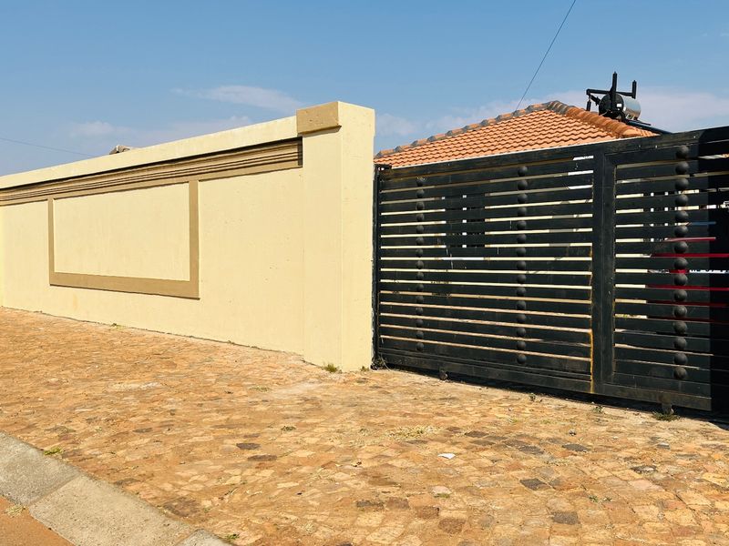Front view of the property featuring a perimeter wall, a black metal sliding gate, and a paved driveway entrance.