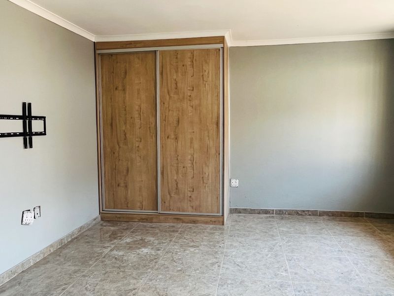 A clean, empty bedroom featuring tiled flooring, a modern wood-finish built-in wardrobe, and security bars on the window.
