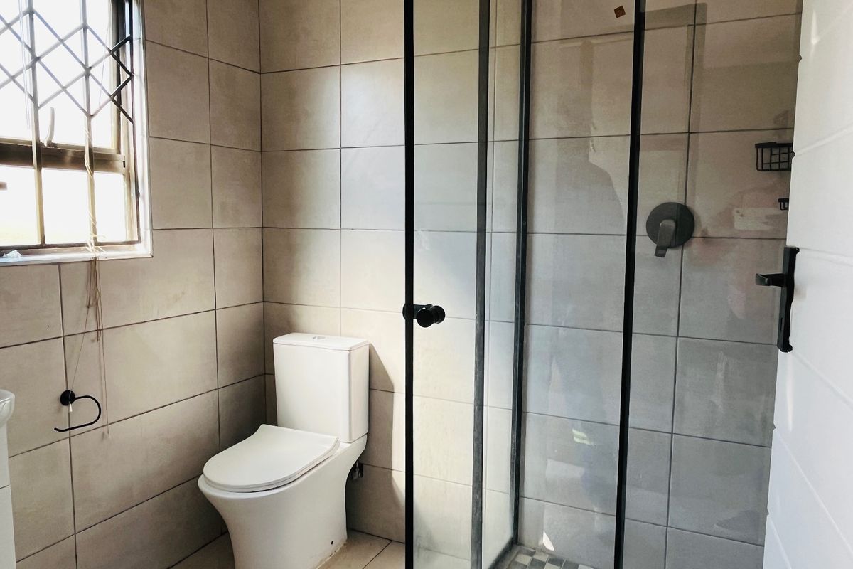 Modern bathroom featuring a walk-in shower with black-framed glass enclosure, neutral wall tiling, and a contemporary toilet.