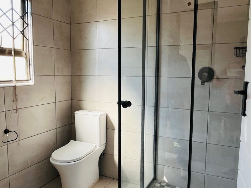 Modern bathroom featuring a walk-in shower with black-framed glass enclosure, neutral wall tiling, and a contemporary toilet.