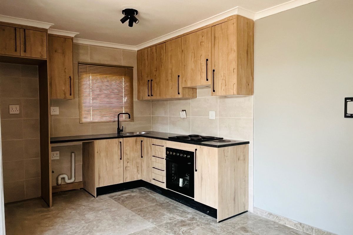 Modern kitchen featuring light wood-look cabinetry, dark countertops, built-in oven and hob, tiled backsplash, and neutral floor tiles in an open-plan layout.
