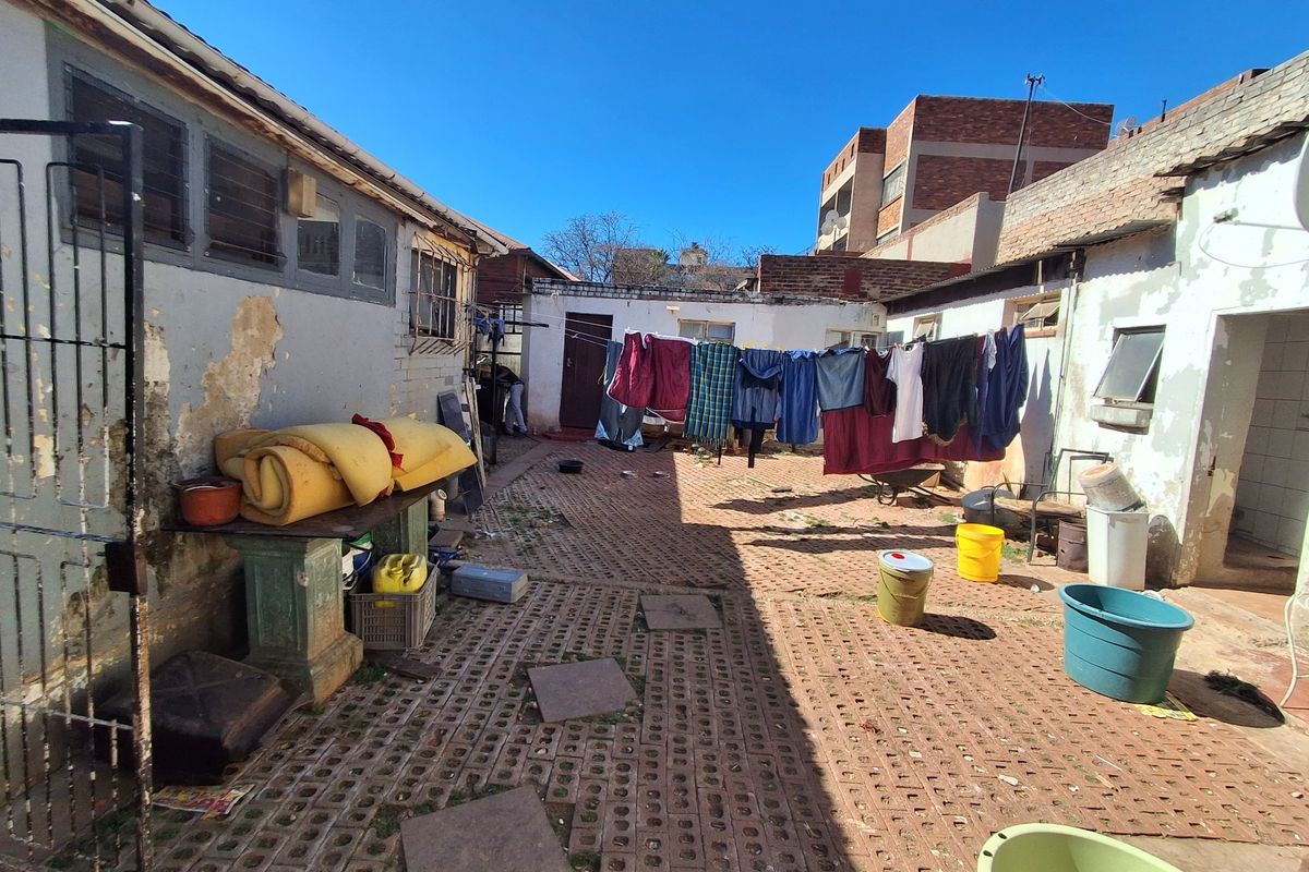 Rear courtyard area featuring brick paving and masonry walls, currently showing significant signs of wear and requiring maintenance to the exterior finishes.