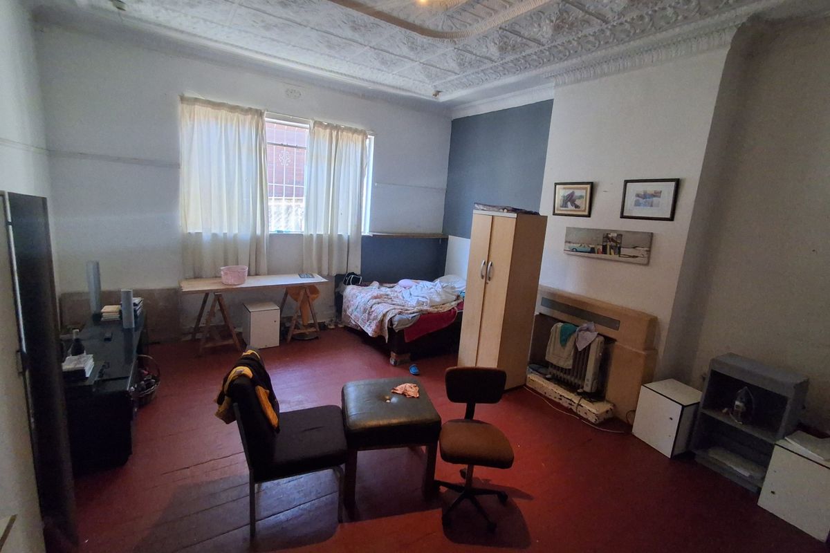 A bedroom featuring an ornate period plaster ceiling, ceiling rose, and a built-in fireplace surround, requiring cosmetic updates to the flooring and wall finishes.