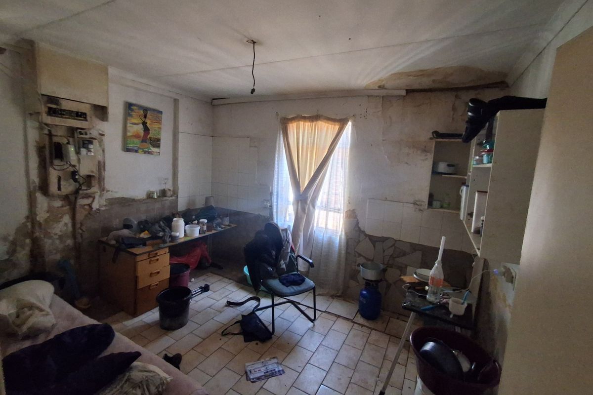A kitchen space in need of significant renovation, featuring tiled floors and walls, with visible signs of water damage and deteriorating wall finishes.