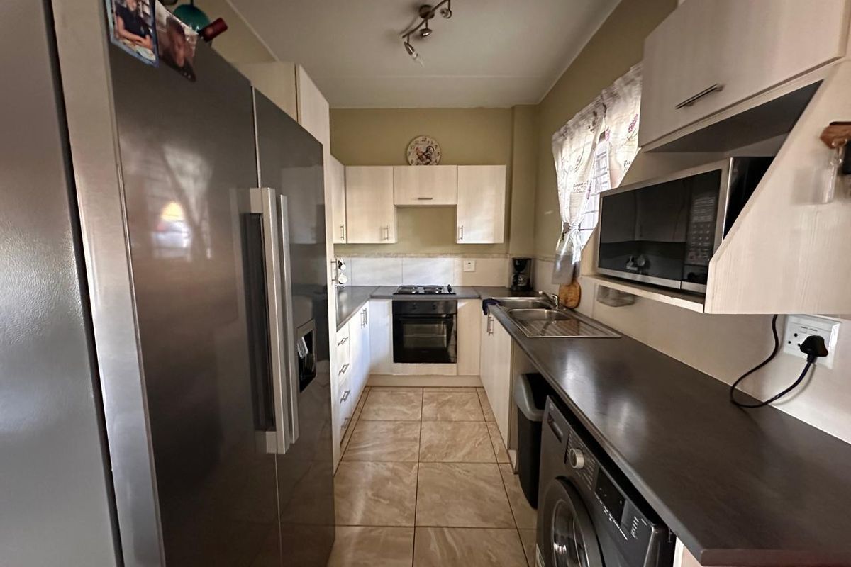 A functional galley-style kitchen featuring built-in cabinetry, laminate countertops, a built-in oven with hob, and integrated microwave space with tiled flooring.