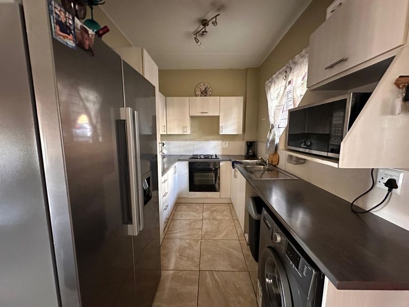 A functional galley-style kitchen featuring built-in cabinetry, laminate countertops, a built-in oven with hob, and integrated microwave space with tiled flooring.