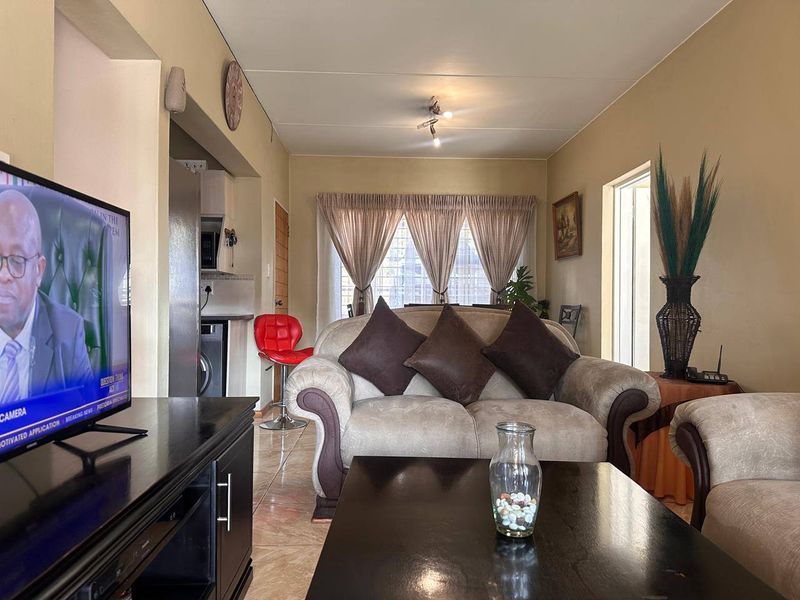 Open-plan living area featuring tiled flooring and a connected kitchen space with built-in cabinetry and sink.