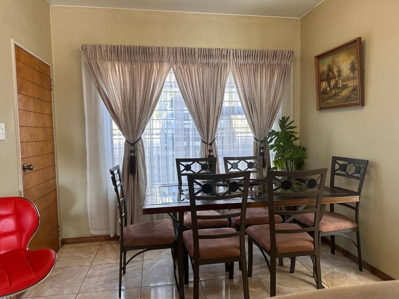 A dining room featuring tiled flooring, a large window with security bars, and a wooden door.