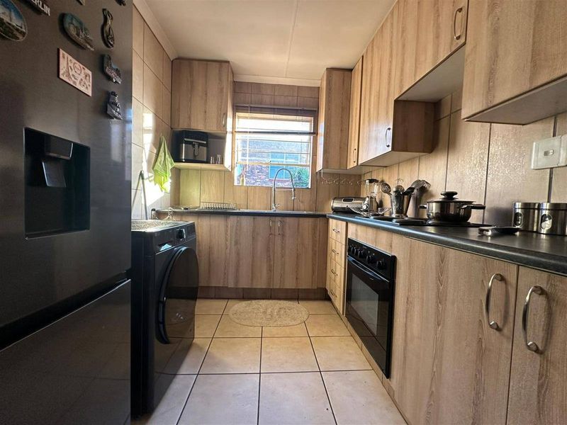 A functional galley-style kitchen featuring wood-look laminate cabinetry, dark countertops, built-in oven, and tiled finishes throughout.
