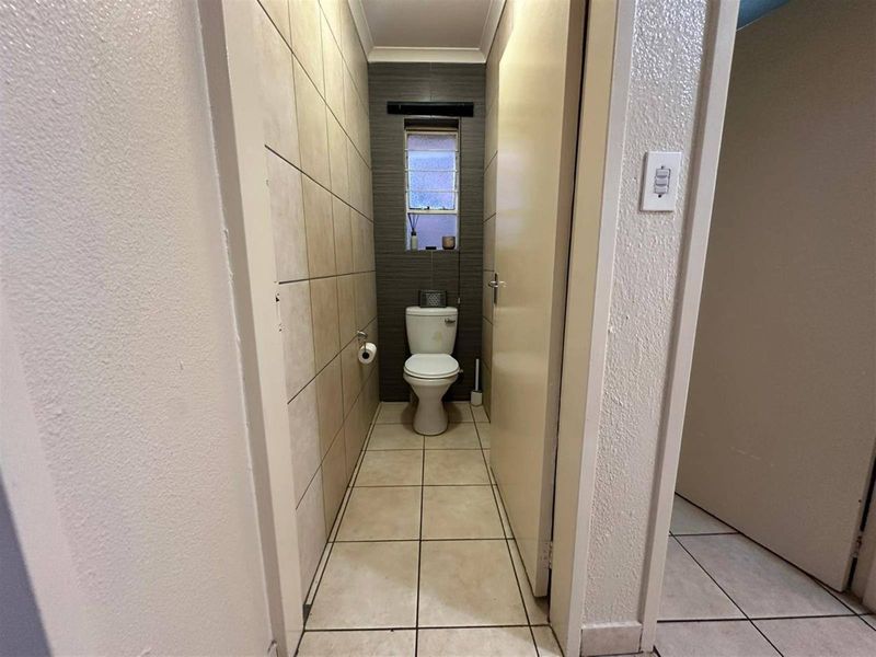 A compact, functional bathroom featuring tiled walls and flooring, a standard toilet, and a small window for natural light.