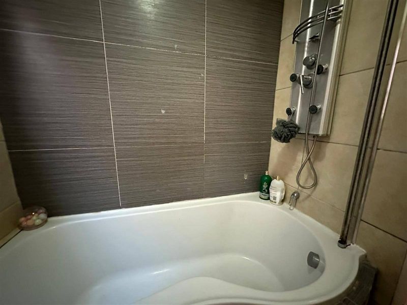 A bathroom featuring a bathtub with a modern shower panel and contrasting dark and light wall tiling.