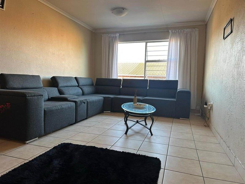 A living room featuring tiled flooring, a large window with security bars, and neutral wall finishes.