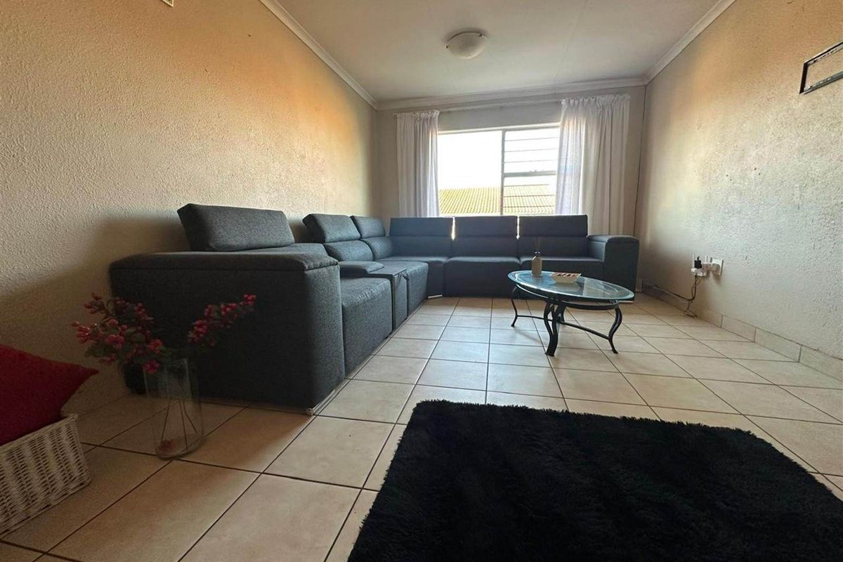 A living room featuring tiled flooring, a large window with curtains, and coved ceiling detailing.