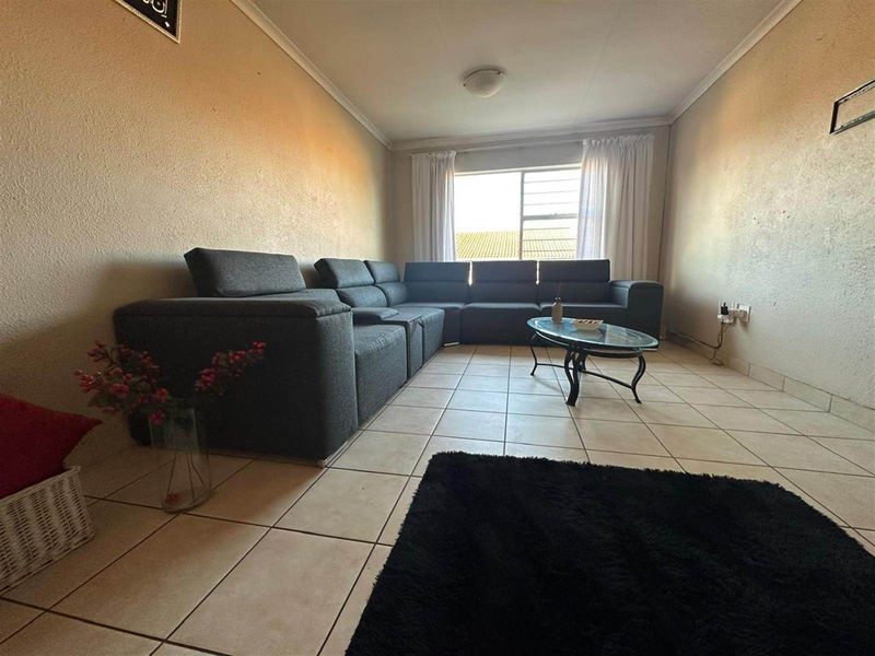 A living room featuring tiled flooring, a large window with curtains, and coved ceiling detailing.