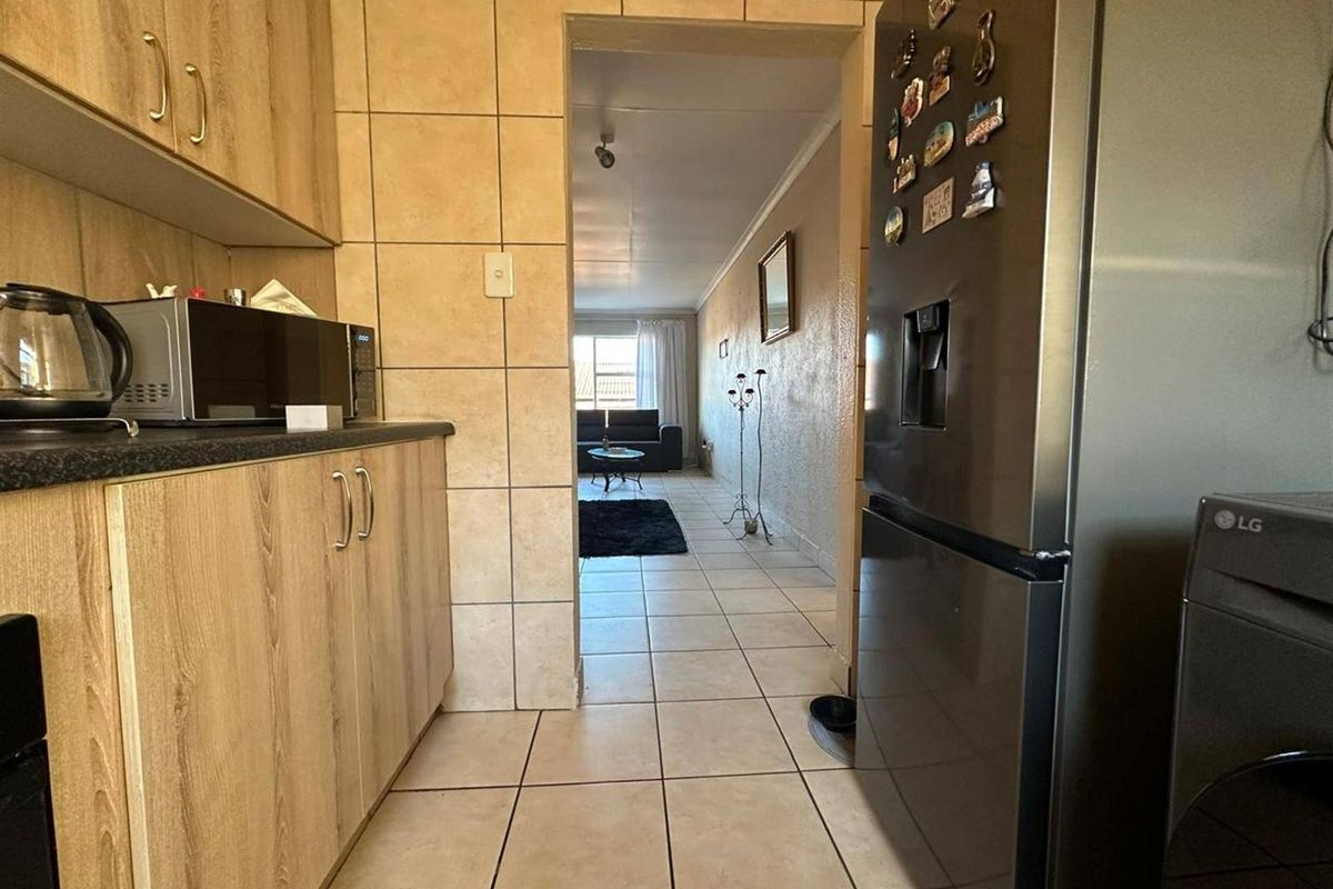 A functional kitchen featuring laminate cabinetry, tiled splashbacks, and tiled flooring, with a direct view through to the adjacent living area.