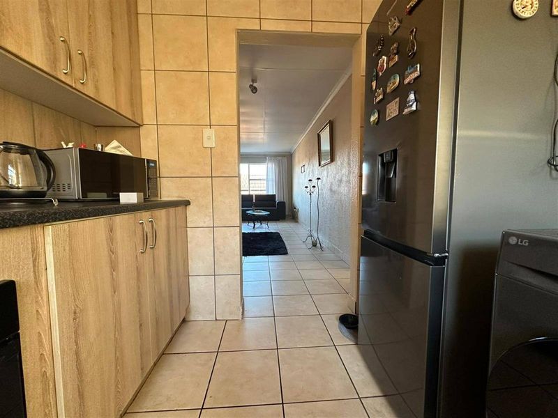 A functional kitchen featuring laminate cabinetry, tiled splashbacks, and tiled flooring, with a direct view through to the adjacent living area.