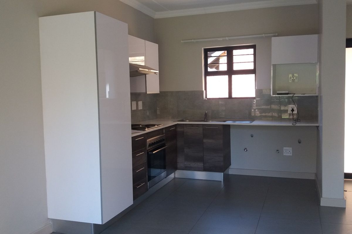 Modern kitchen featuring sleek two-tone cabinetry, built-in oven and hob, tiled splashback, and neutral floor tiles in an open-plan layout.
