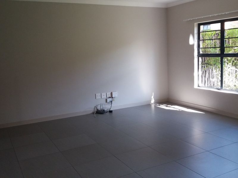 A spacious, empty living area featuring neutral tiled flooring, a staircase with a modern metal railing, and a window with security bars.