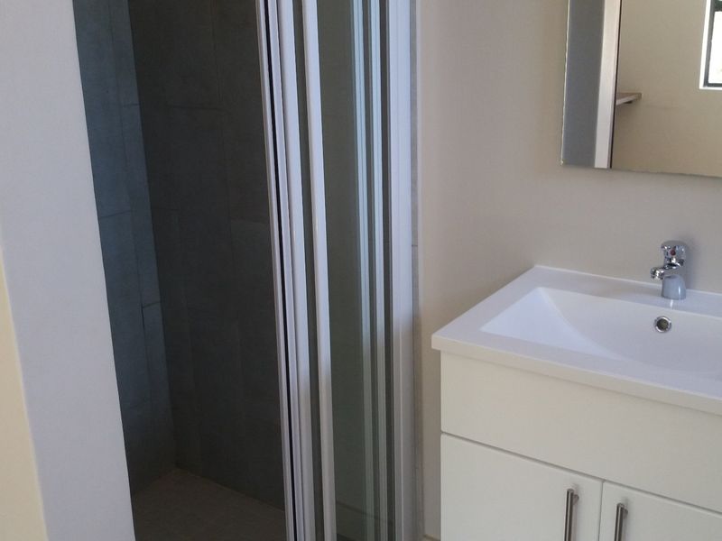 A clean, modern bathroom featuring a white vanity with basin, mixer tap, wall mirror, and a glass-enclosed shower.