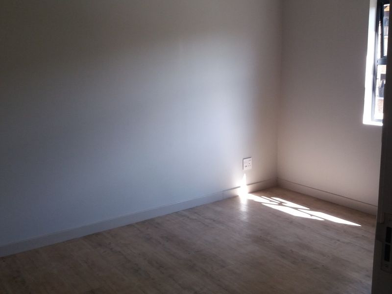 An empty bedroom featuring light-toned laminate flooring, neutral walls, and a window allowing natural light.